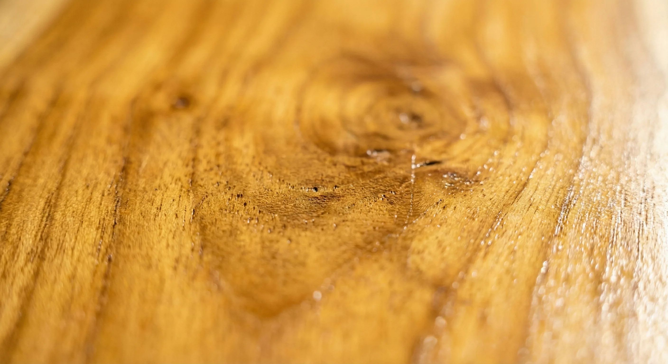 Close-up of Grade-A teak wood grain showing warm golden-honey color and natural oil sheen